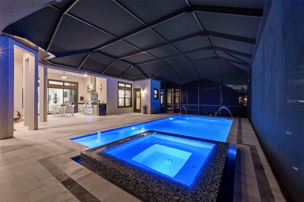 A screened-in patio features a swimming pool, a raised spa, and an outdoor kitchen area — 34135 TOMPION WAY, WESLEY CHAPEL, FL