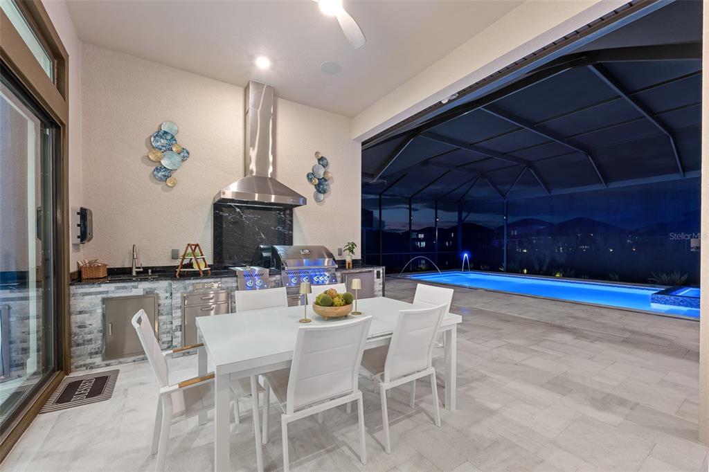 An outdoor kitchen and dining area overlook a screened-in swimming pool at night — 34135 TOMPION WAY, WESLEY CHAPEL, FL