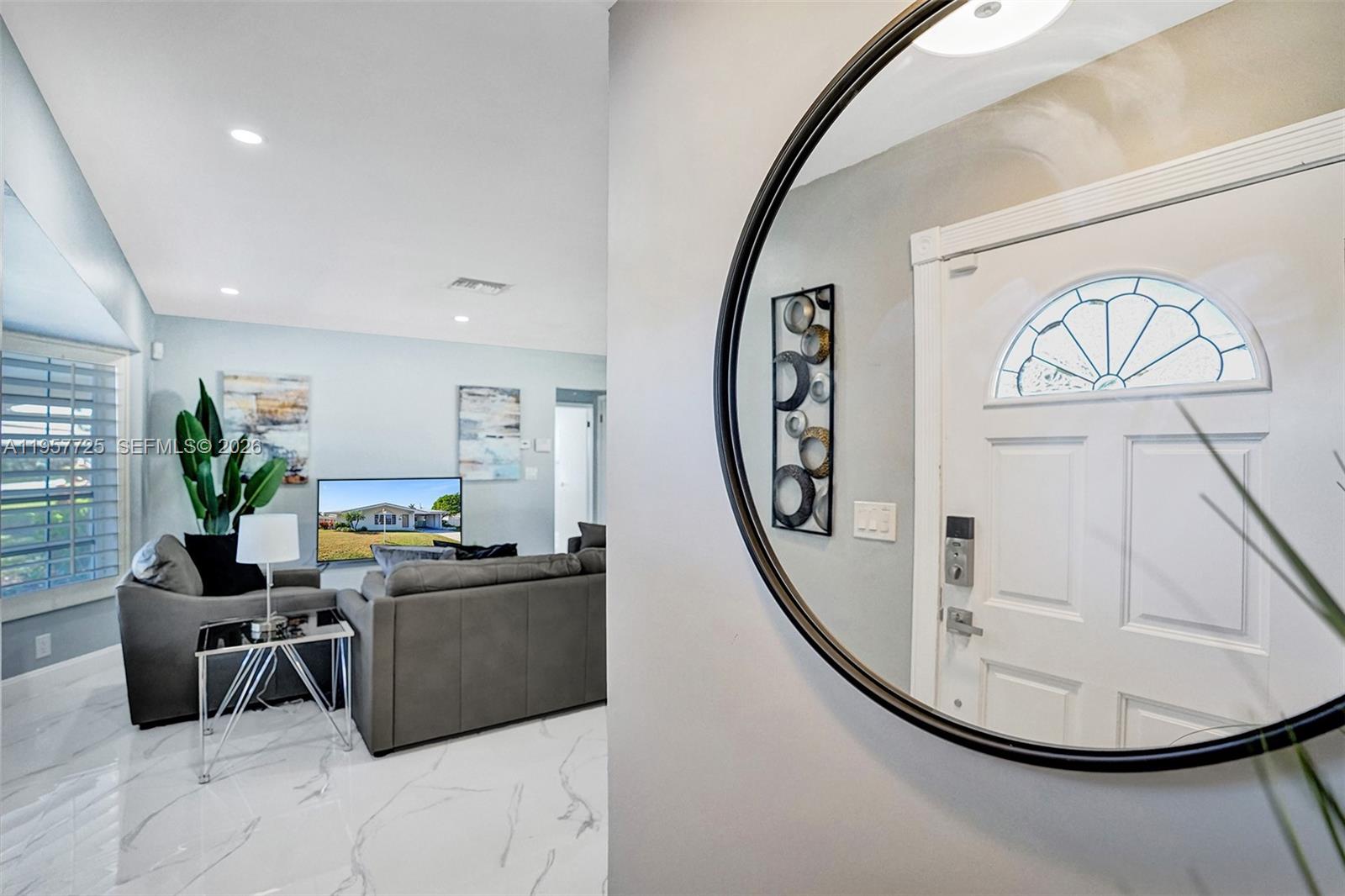 A living room with gray furniture and marble floors is viewed through a circular mirror — 477 SE 17th Ter, Deerfield Beach FL 33441, DEERFIELD BEACH, FL