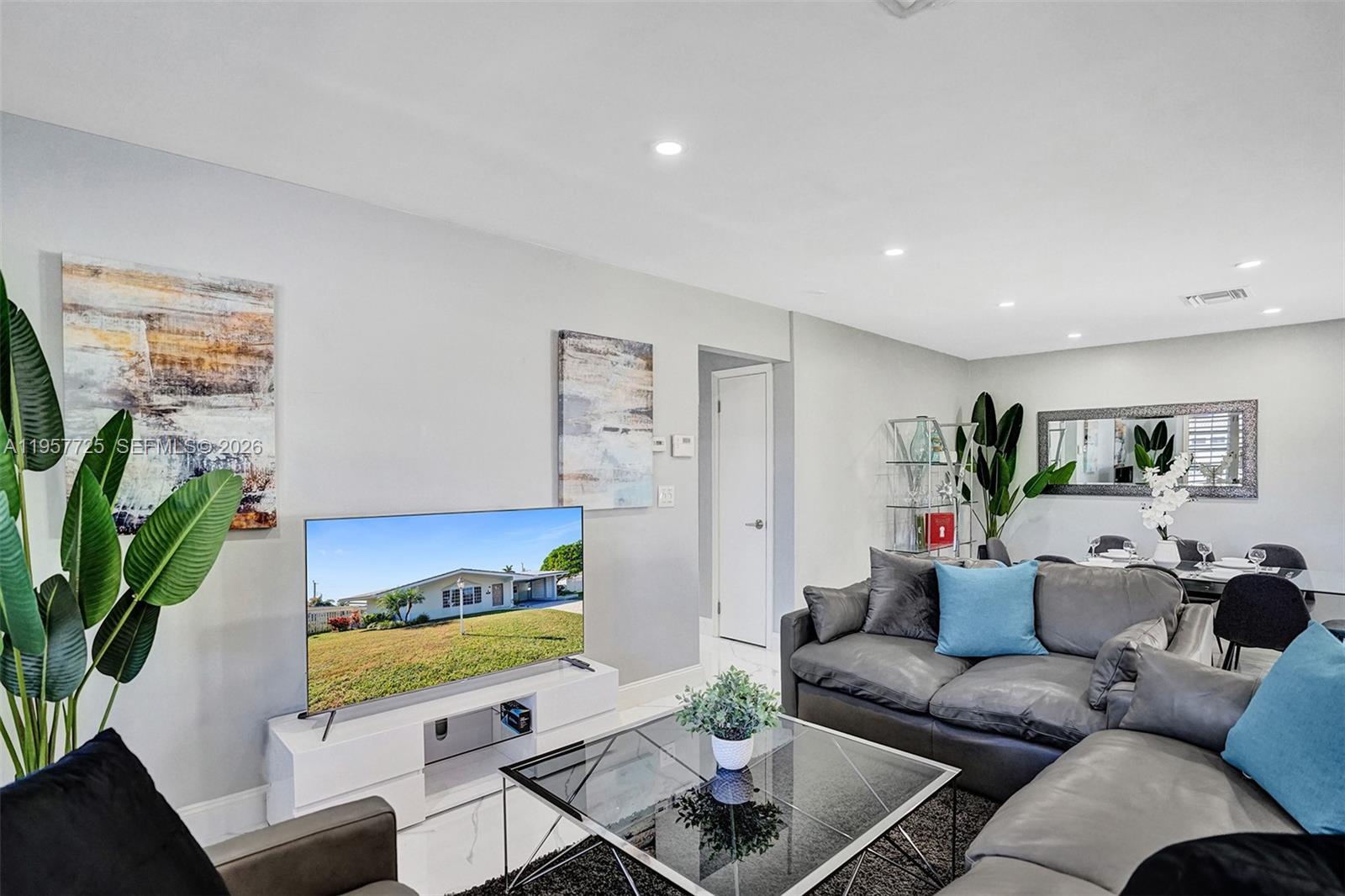 A living room features a grey sectional sofa, glass coffee table, and a wall-mounted television — 477 SE 17th Ter, Deerfield Beach FL 33441, DEERFIELD BEACH, FL