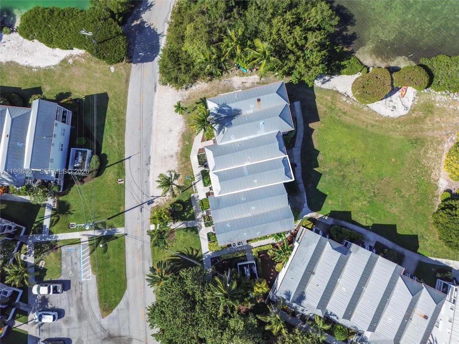 An aerial view shows several multi-story buildings with metal roofs surrounded by trees and grass — 5101 Sunset Village Dr, Duck FL 33050, DUCK, FL