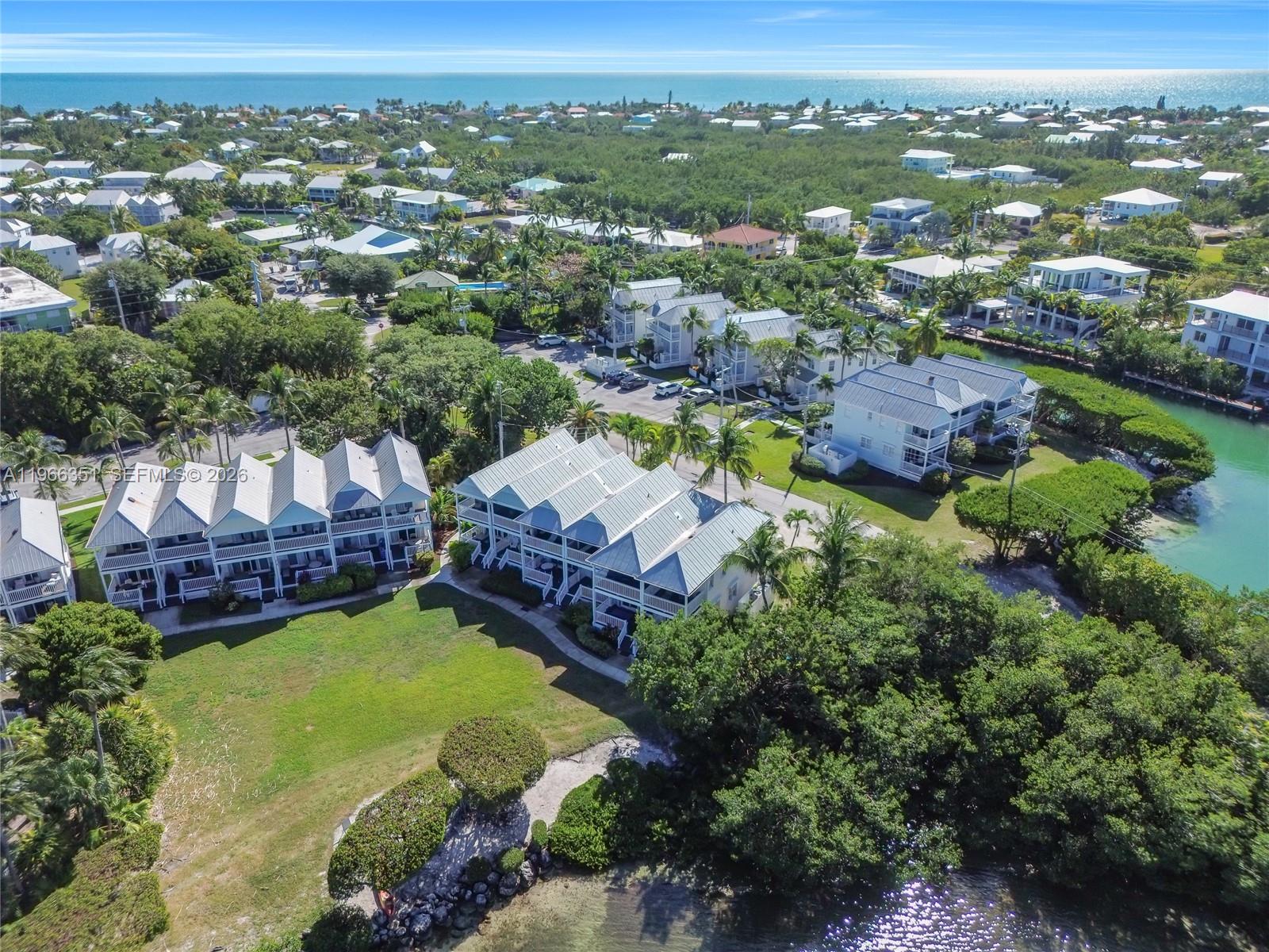 An aerial view shows multiple multi-story residential buildings surrounded by lush trees and water — 5101 Sunset Village Dr, Duck FL 33050, DUCK, FL