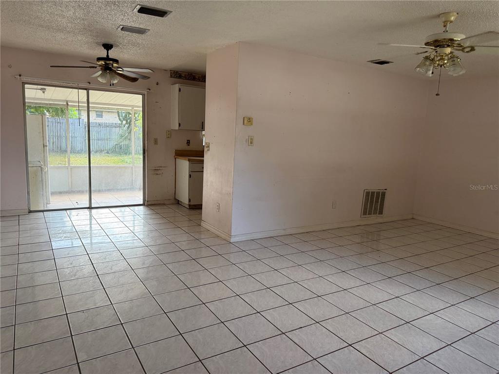 An open-concept living and dining area features white tile flooring and a sliding glass door — 2479 KIMBERLY DRIVE, DELTONA, FL