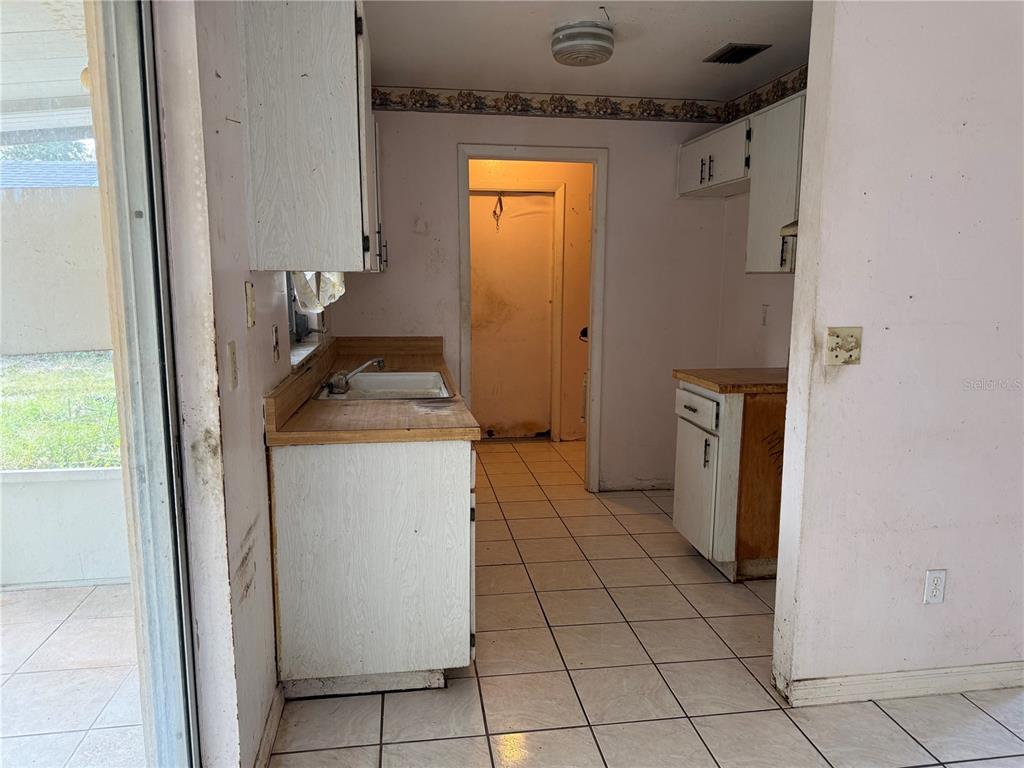 A kitchen with white cabinets, laminate countertops, tiled floors, and a doorway leading outside — 2479 KIMBERLY DRIVE, DELTONA, FL