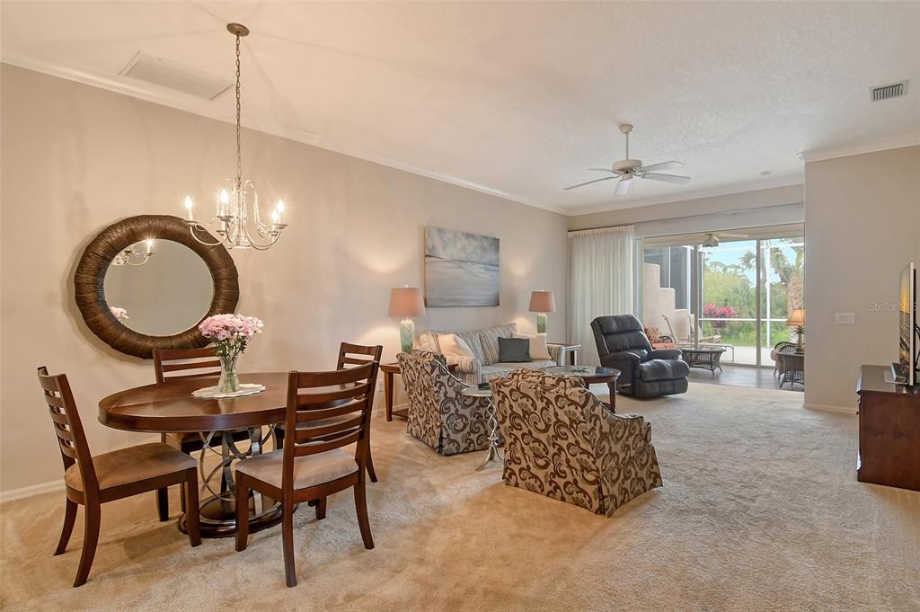 An open-concept living and dining area features carpeted floors, a round table, and sliding doors — 9411 FOREST HILLS CIRCLE, SARASOTA, FL