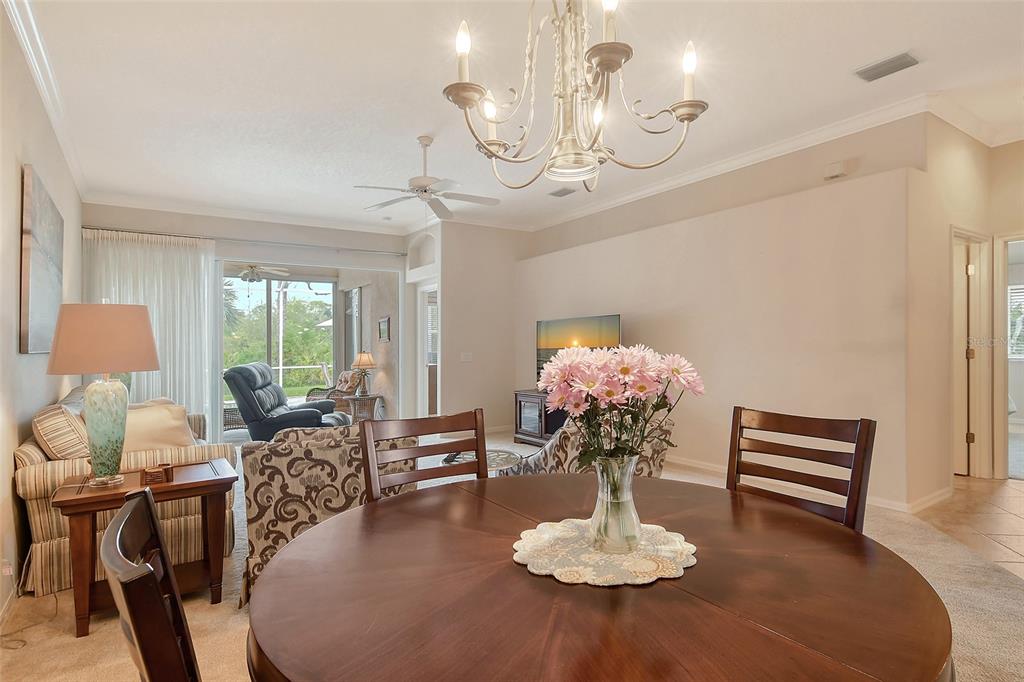 A dining area with a round wooden table and chandelier opens into a living room — 9411 FOREST HILLS CIRCLE, SARASOTA, FL