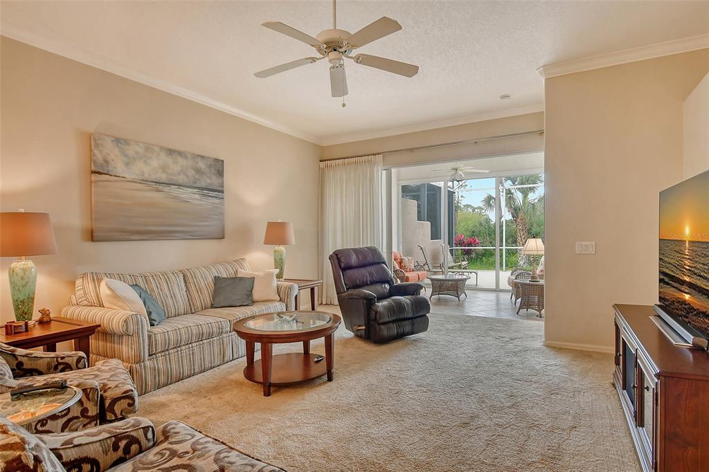 A living room with beige carpet, a striped sofa, a recliner, and a sliding glass door — 9411 FOREST HILLS CIRCLE, SARASOTA, FL