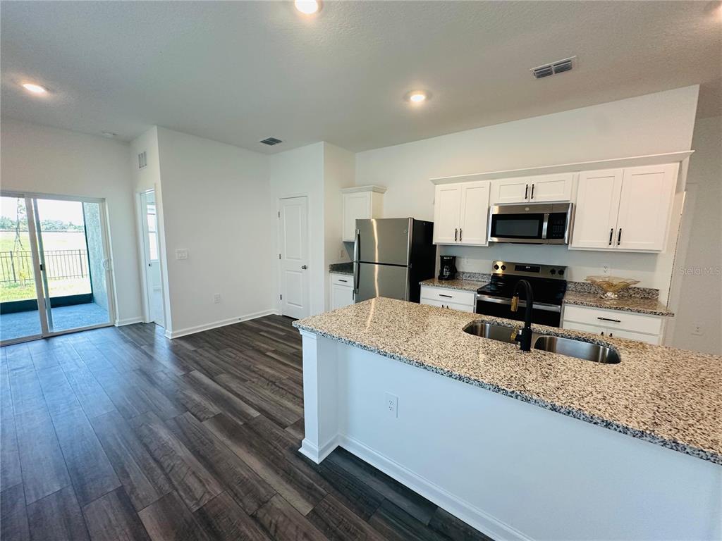 A kitchen with white cabinets, granite countertops, stainless steel appliances, and dark wood-look flooring — 10473 CURVING CREEK LOOP, PARRISH, FL