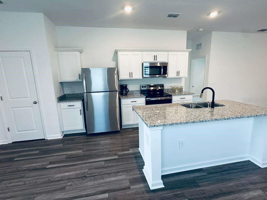 A kitchen features white cabinets, stainless steel appliances, granite countertops, and a center island — 10473 CURVING CREEK LOOP, PARRISH, FL