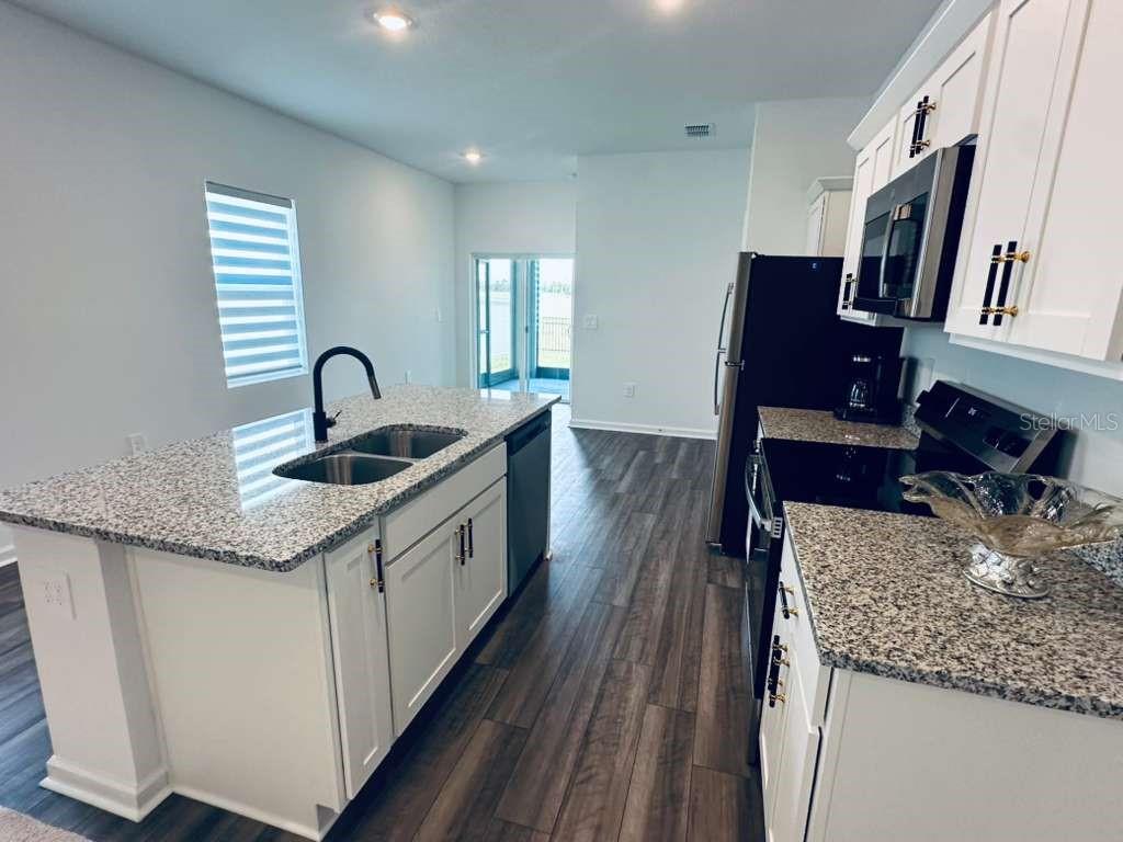 A kitchen features white cabinets, granite countertops, a center island, and dark wood-look flooring — 10473 CURVING CREEK LOOP, PARRISH, FL