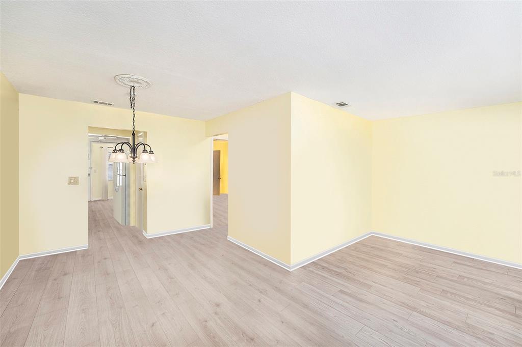 An empty room with pale yellow walls, light wood-look flooring, and a hanging chandelier — 5216 81ST STREET N UNIT 2, ST PETERSBURG, FL