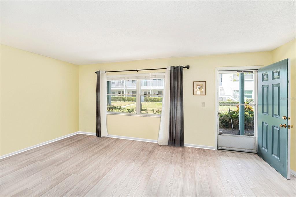 An empty room with light wood-look flooring, pale yellow walls, a window, and a door — 5216 81ST STREET N UNIT 2, ST PETERSBURG, FL