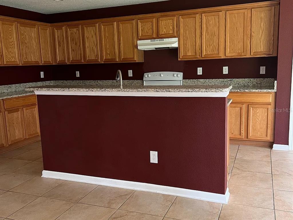 A kitchen features oak cabinets, granite countertops, and a dark red island with a sink — 70 ROLLINS LANE, PALM COAST, FL