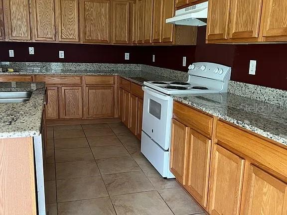 A kitchen features oak cabinets, granite countertops, tile flooring, and a white electric range — 70 ROLLINS LANE, PALM COAST, FL