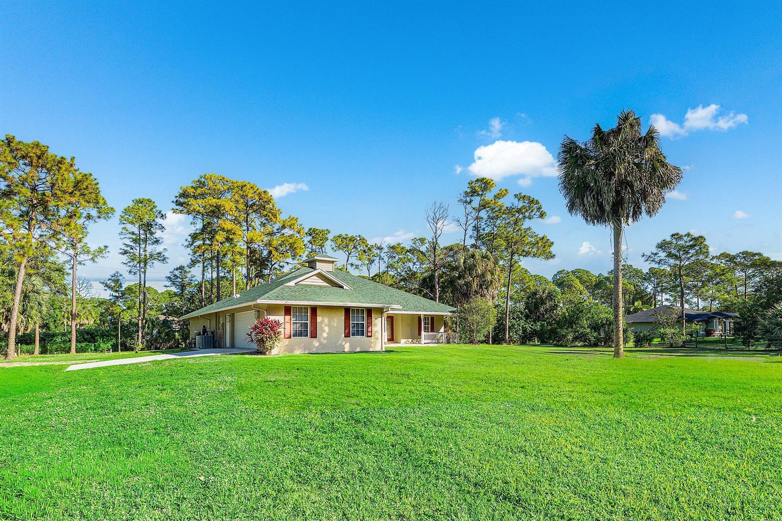 A single-story house with a green roof and a large lawn under a blue sky — 17109 Murcott Boulevard, FL 33470, FL