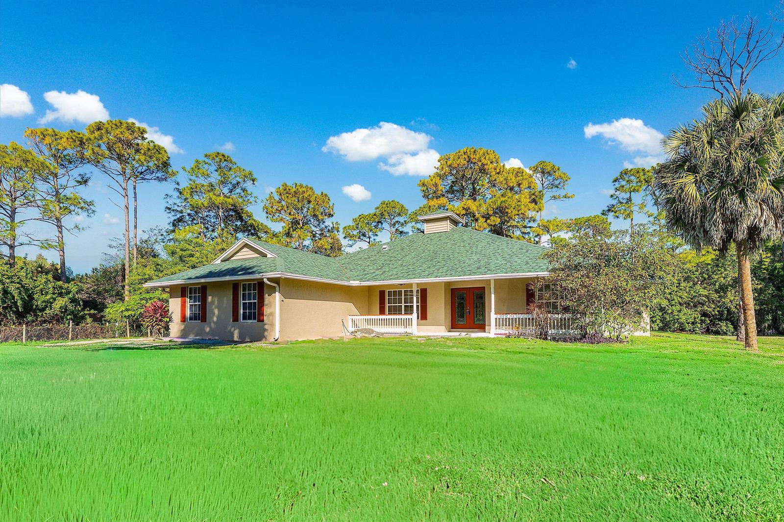 A single-story house with a green roof and tan exterior sits on a grassy lawn — 17109 Murcott Boulevard, FL 33470, FL