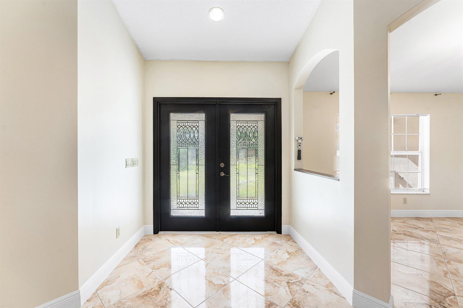 An entryway features double glass-paneled doors, light-colored walls, and polished marble-look tile flooring — 17109 Murcott Boulevard, FL 33470, FL