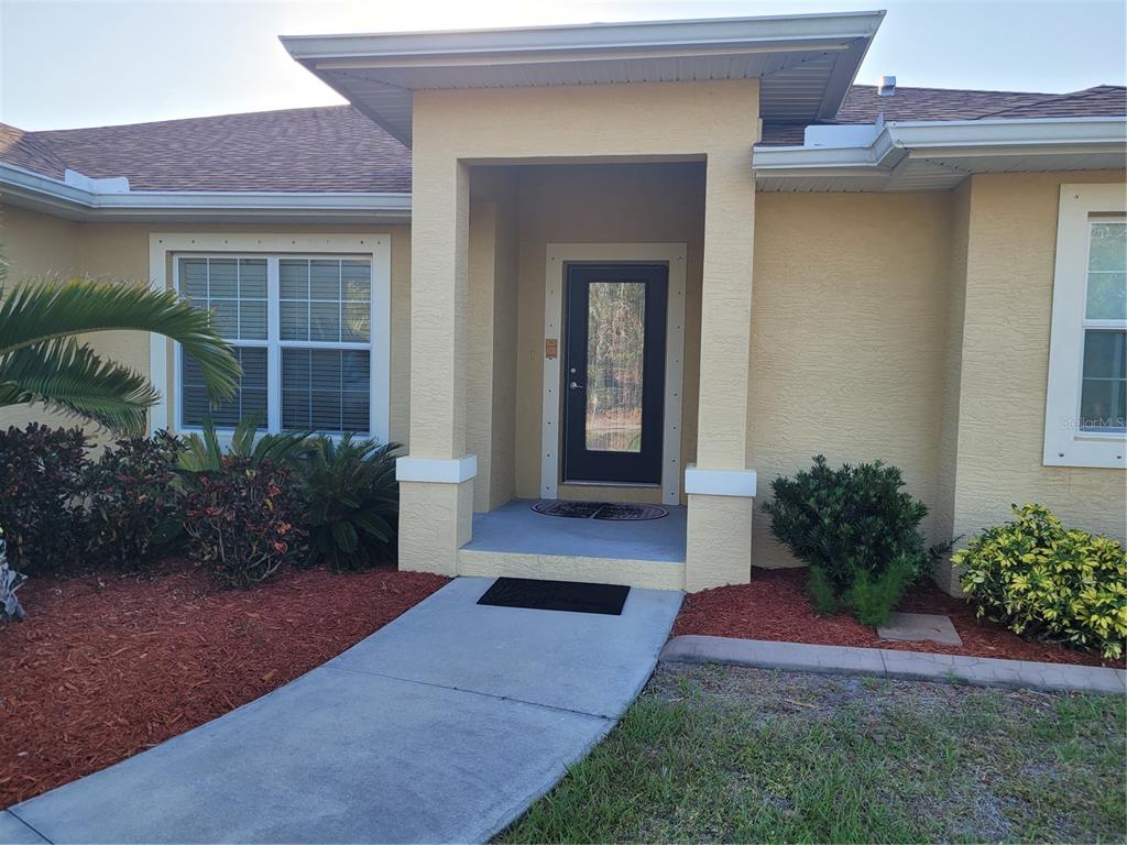 A yellow stucco house exterior features a covered entryway with a dark glass front door — 9458 MODESTO CIRCLE, PORT CHARLOTTE, FL