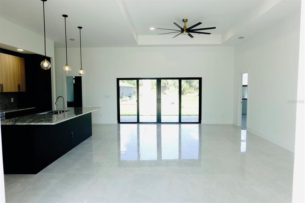A modern kitchen with a dark island and pendant lights opens into a spacious living area — 700 BISCAYNE DRIVE, PORT CHARLOTTE, FL