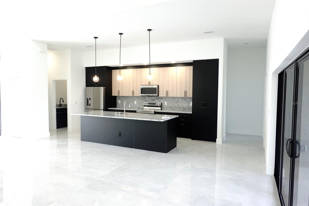 A modern kitchen features a black island, two-tone cabinetry, stainless steel appliances, and tile flooring — 700 BISCAYNE DRIVE, PORT CHARLOTTE, FL