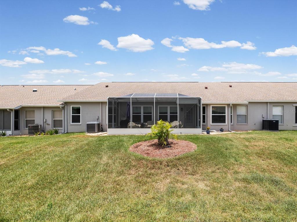 The rear exterior of a single-story home features a screened-in patio and a grassy yard — 18730 WORTHINGTON DRIVE, HUDSON, FL
