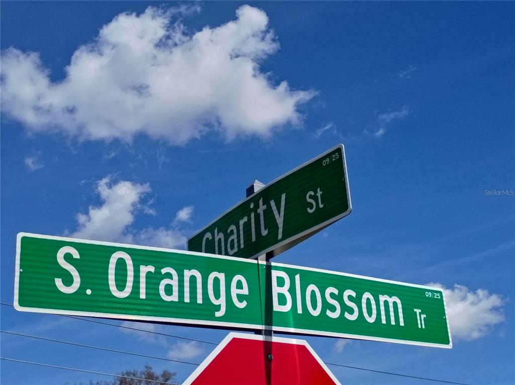 A street sign intersection shows Charity St and S. Orange Blossom Tr against a blue sky — 5574 S ORANGE BLOSSOM TRAIL, INTERCESSION CITY, FL
