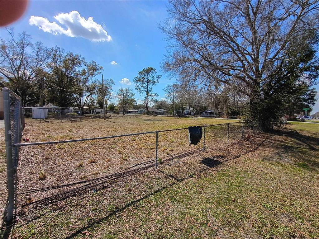 A chain-link fence encloses a vacant, grassy lot with several large trees under a blue sky — 5574 S ORANGE BLOSSOM TRAIL, INTERCESSION CITY, FL