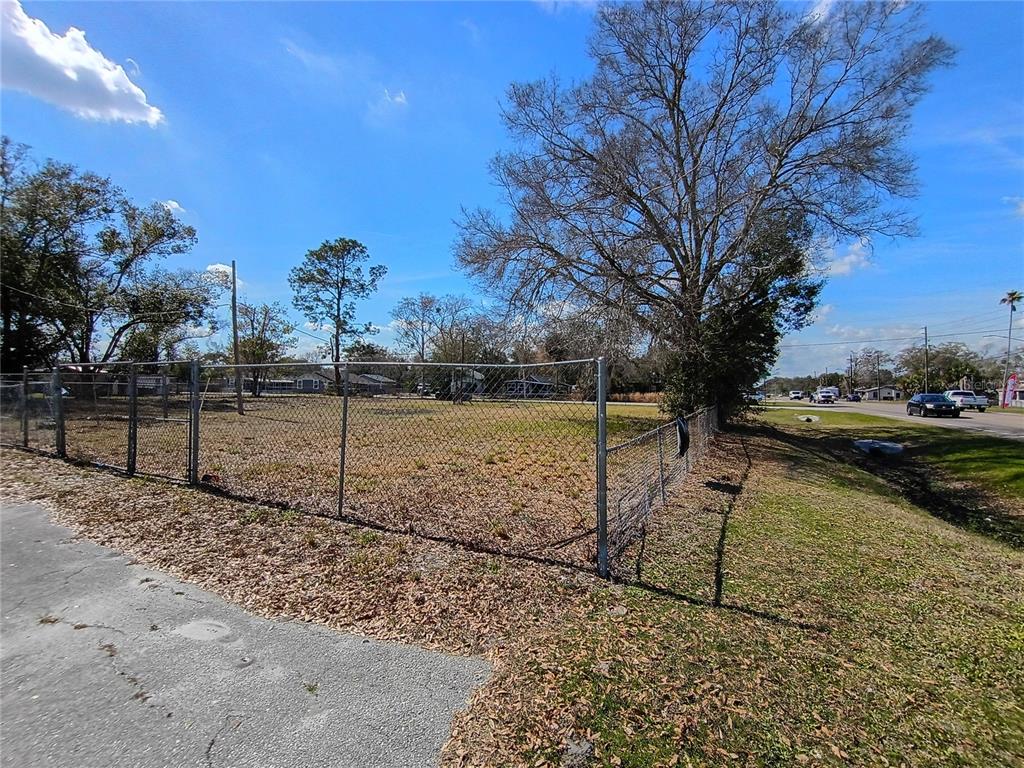 A chain-link fence encloses a vacant, grassy lot with several large trees under a blue sky — 5574 S ORANGE BLOSSOM TRAIL, INTERCESSION CITY, FL