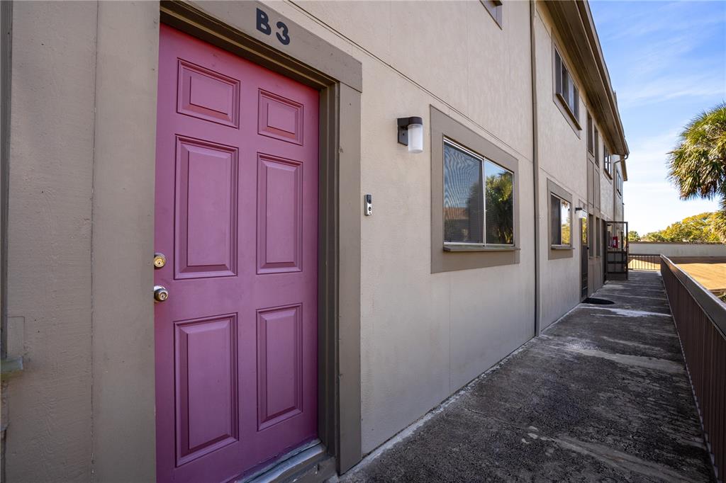 A pink front door labeled B3 opens onto an outdoor concrete walkway of a building — 6315 NEWTOWN CIRCLE UNIT 15B3, TAMPA, FL
