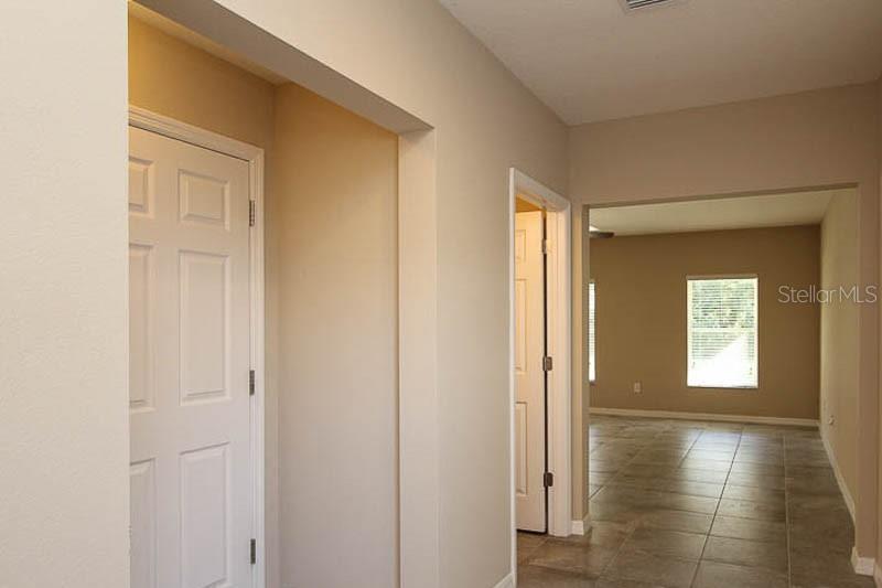 A hallway with tiled floors leads to an open room with beige walls and windows — 5206 BANNISTER PARK LANE, LITHIA, FL