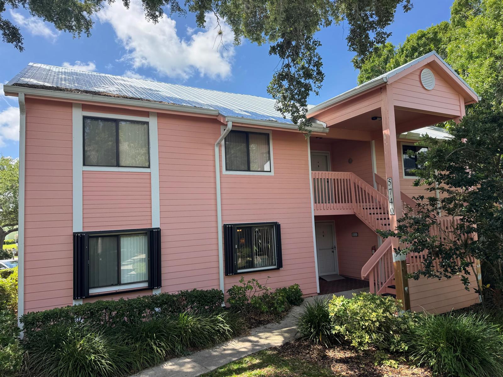 A two-story pink building with a metal roof, exterior staircase, and surrounding landscaping — SEBASTIAN, FL