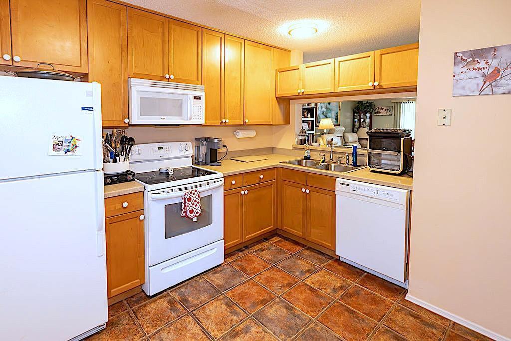 A kitchen with light wood cabinets, white appliances, and brown tile flooring — SEBASTIAN, FL