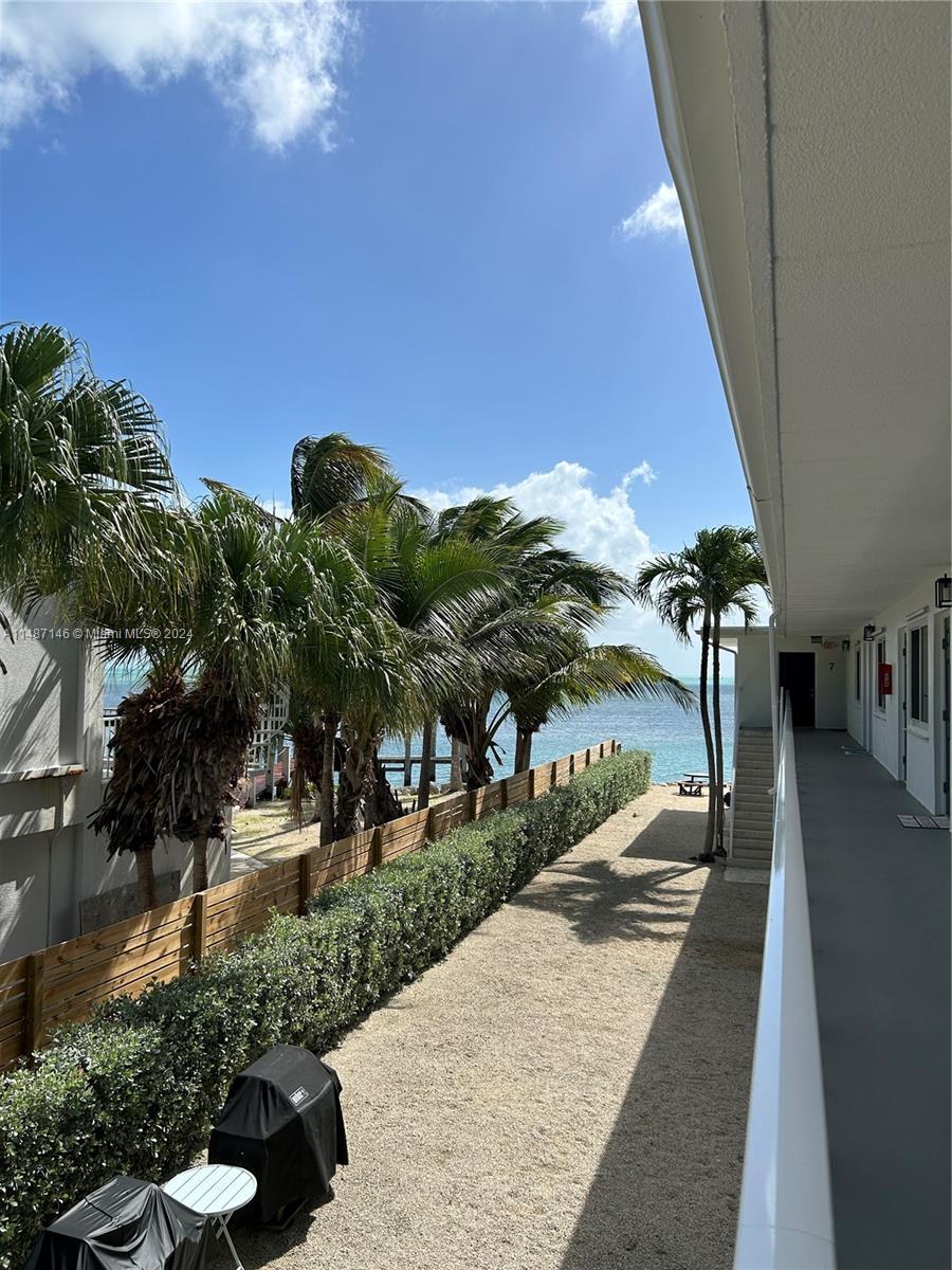 An outdoor walkway overlooks a gravel yard, palm trees, and the ocean — 1215 97th Street Ocean # 11, Marathon FL 33050, MARATHON, FL