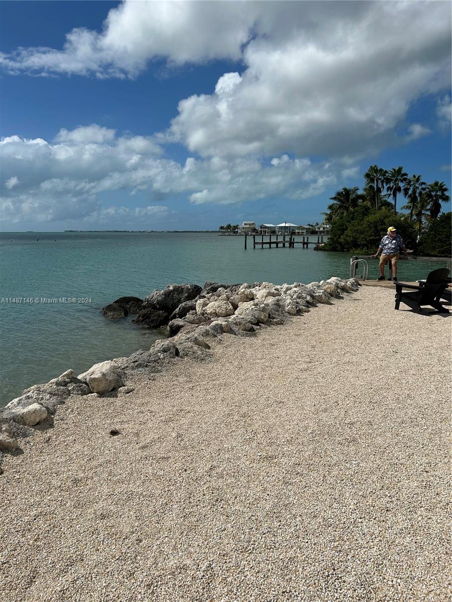 A man sits on a wooden deck overlooking a rocky shoreline and the ocean — 1215 97th Street Ocean # 11, Marathon FL 33050, MARATHON, FL