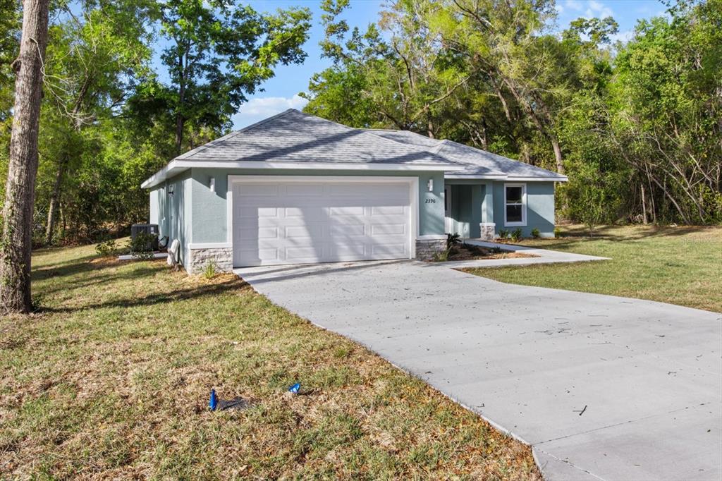 A single-story house with a light green exterior, stone accents, and a concrete driveway — 2396 W FAIRWAY LOOP, CITRUS SPRINGS, FL