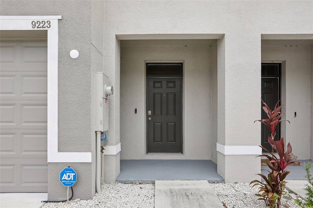 The exterior of a townhouse features a gray garage, a dark front door, and gravel landscaping — 9223 ROCK HARBOUR WAY, TAMPA, FL