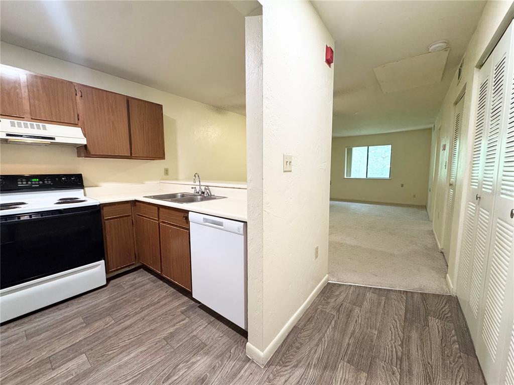 A kitchen with wood cabinets, white appliances, and laminate flooring opens into a carpeted living area — 83 SE 16TH AVENUE UNIT E303, GAINESVILLE, FL