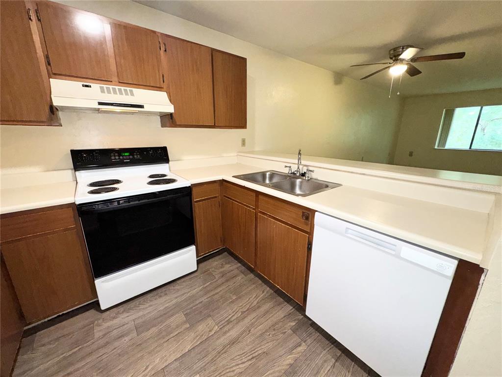 A kitchen features wood cabinets, a white stove, a white dishwasher, and a stainless sink — 83 SE 16TH AVENUE UNIT E303, GAINESVILLE, FL