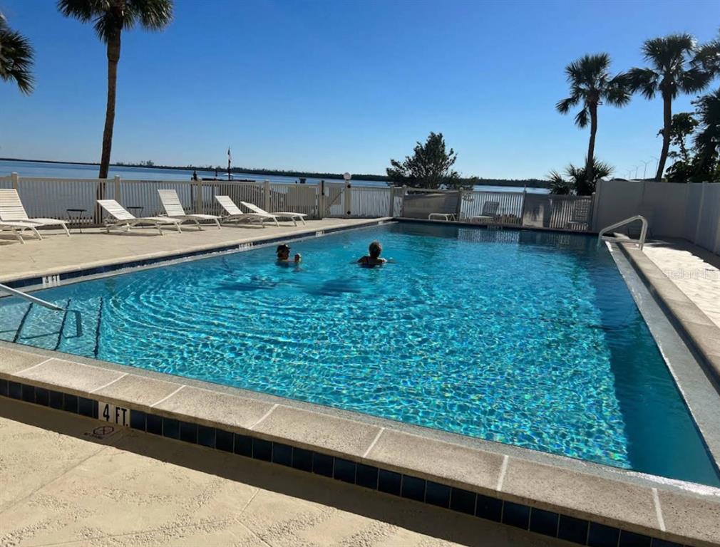 An outdoor swimming pool overlooks a body of water with lounge chairs on the deck — 14459 RIVER BEACH DRIVE UNIT 226, PORT CHARLOTTE, FL