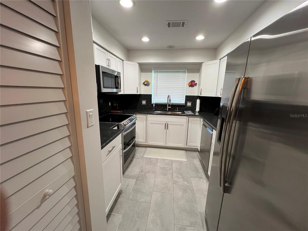 A galley kitchen features white cabinets, dark countertops, stainless steel appliances, and gray tile flooring — 14459 RIVER BEACH DRIVE UNIT 226, PORT CHARLOTTE, FL