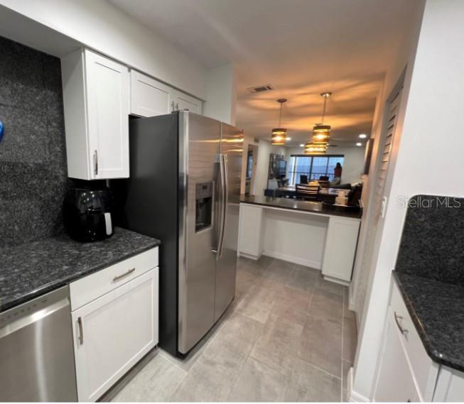 A kitchen with white cabinets, dark granite countertops, and stainless steel appliances overlooks a dining area — 14459 RIVER BEACH DRIVE UNIT 226, PORT CHARLOTTE, FL