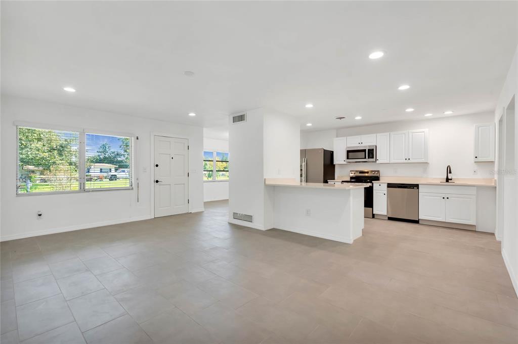 An open-concept kitchen and living area featuring white cabinets, stainless appliances, and light tile flooring — 448 RIDGE DRIVE, SANFORD, FL