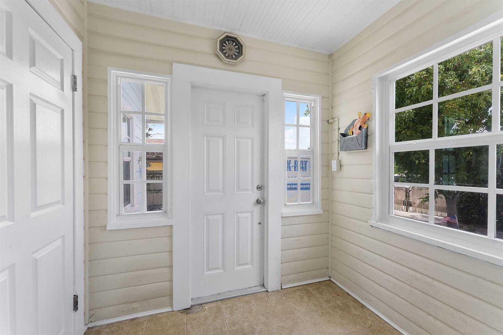 A sunroom features light-colored horizontal siding, a central white door, and tiled flooring — 506 Malverne Road, West Palm Beach FL 33405, WEST PALM BEACH, FL