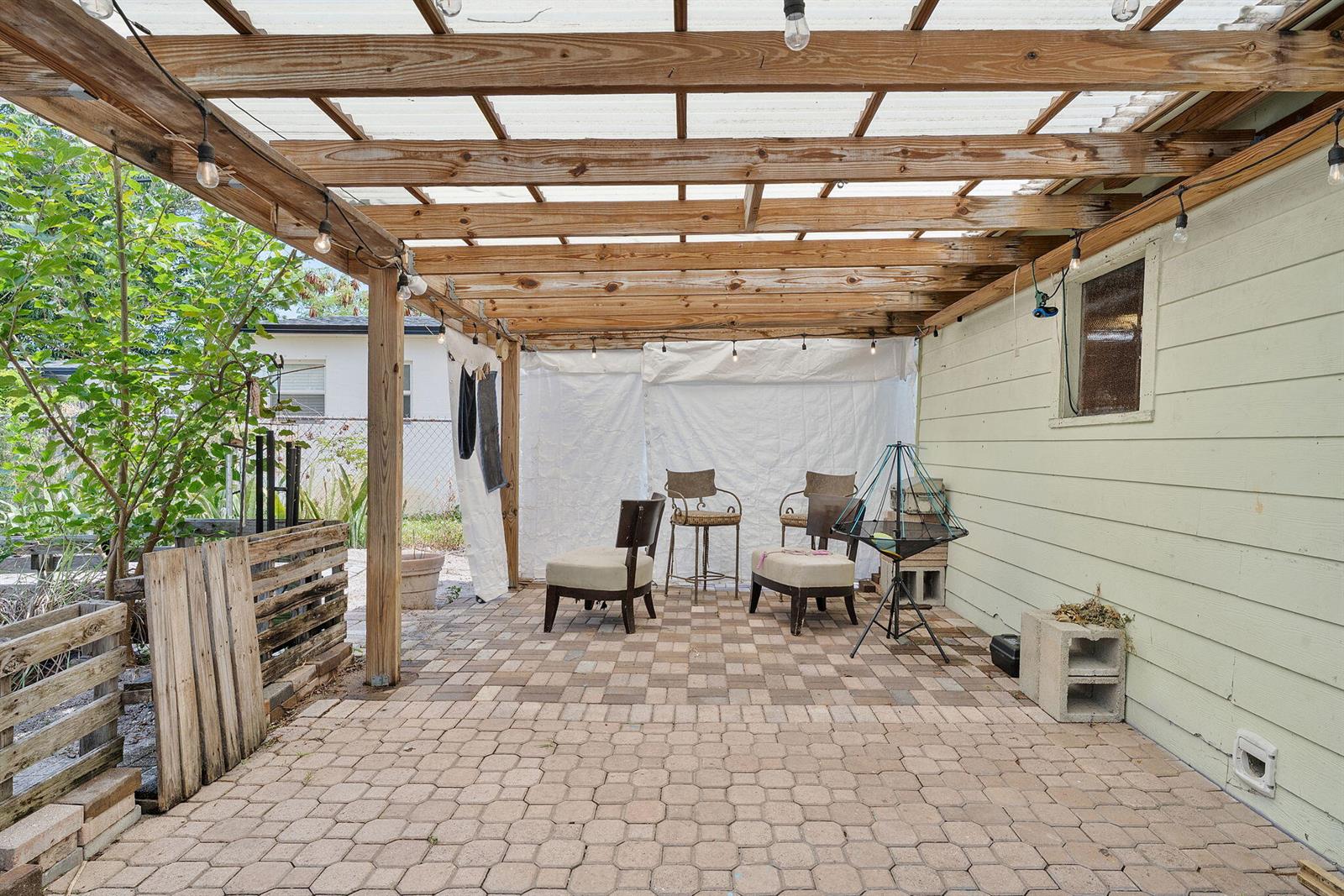A covered outdoor patio features a paver floor, wooden rafters, and several chairs — 506 Malverne Road, West Palm Beach FL 33405, WEST PALM BEACH, FL