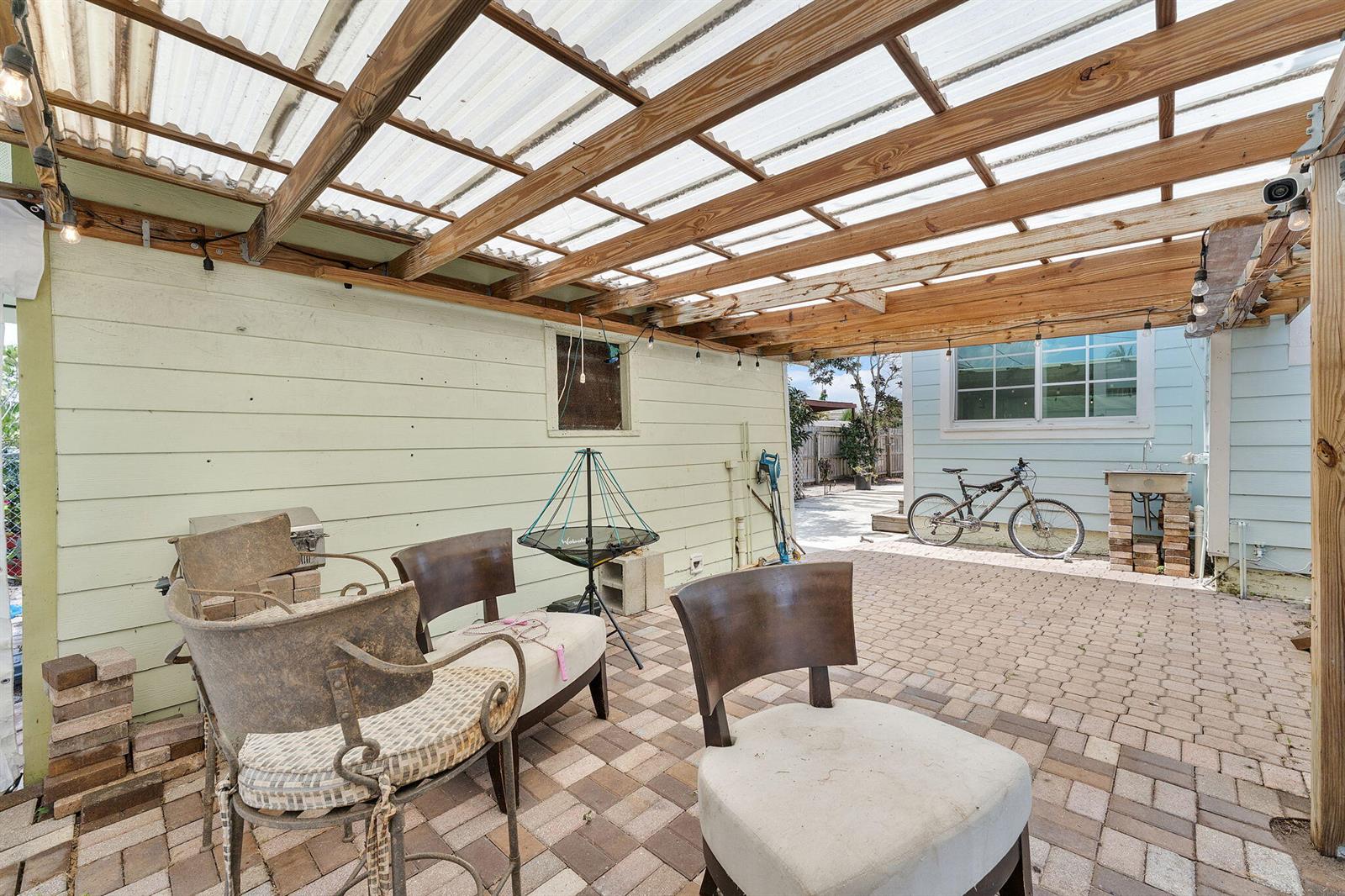 A covered outdoor patio with a translucent roof, brick pavers, and several chairs — 506 Malverne Road, West Palm Beach FL 33405, WEST PALM BEACH, FL