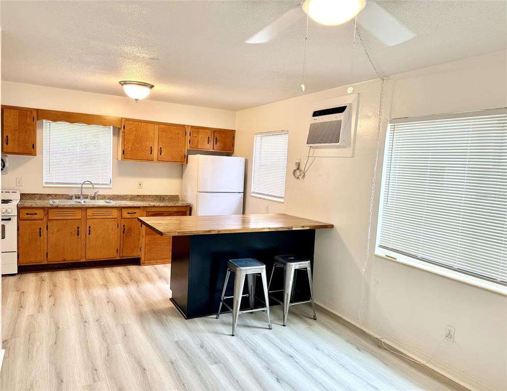 A kitchen features wood cabinets, a black island with two stools, and light-colored flooring — 1135 HIGHLAND STREET N UNIT 3, ST PETERSBURG, FL