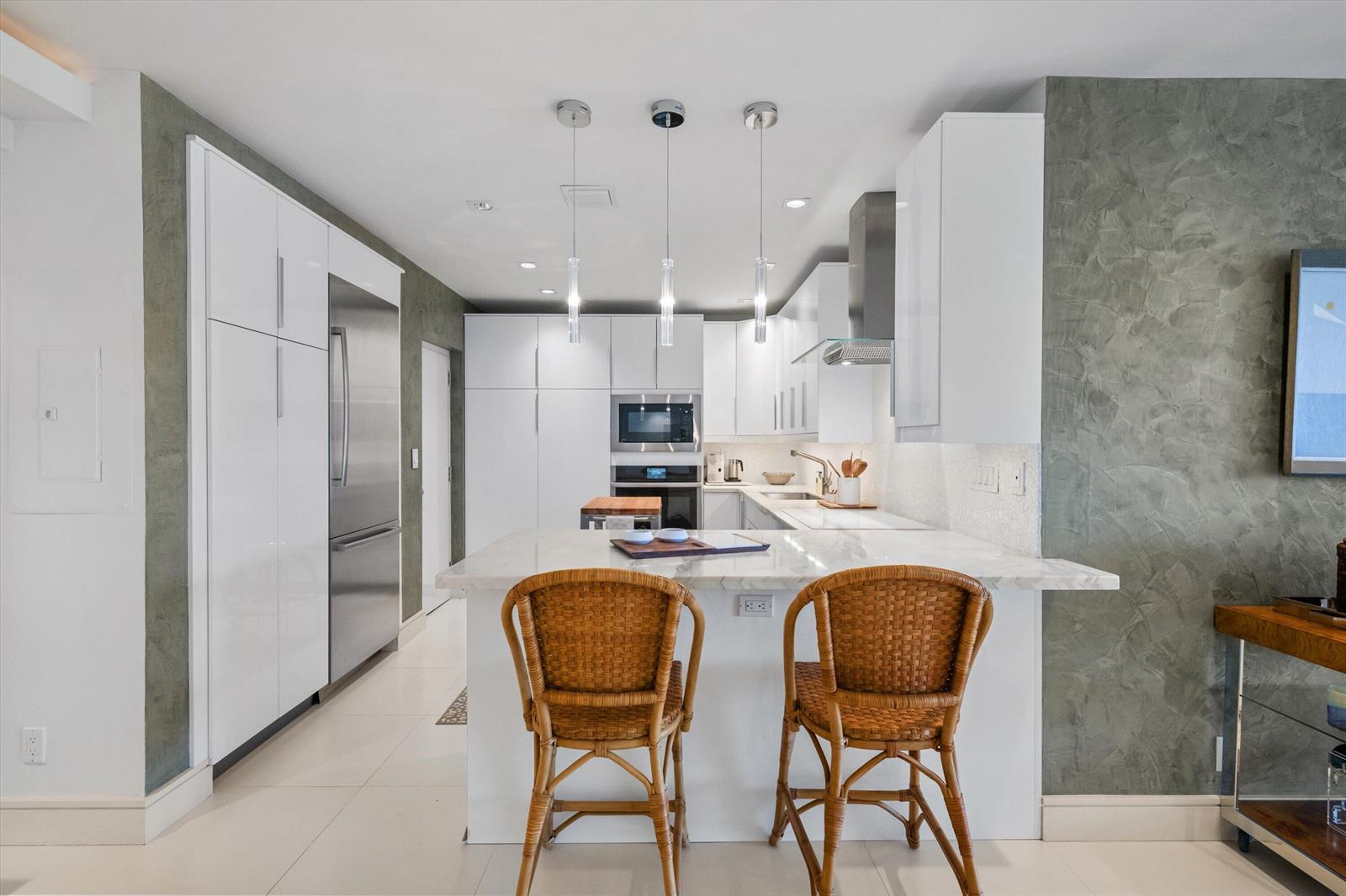 A modern kitchen features white cabinetry, a marble-topped island, and two wicker bar stools — 2275 S Ocean Boulevard, Palm Beach FL 33480, PALM BEACH, FL