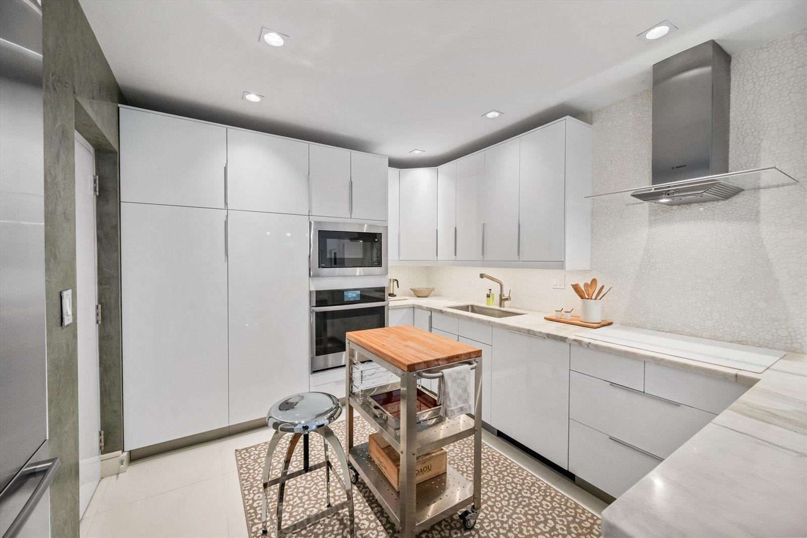 A modern kitchen features white flat-panel cabinetry, stainless steel appliances, and a butcher block island — 2275 S Ocean Boulevard, Palm Beach FL 33480, PALM BEACH, FL