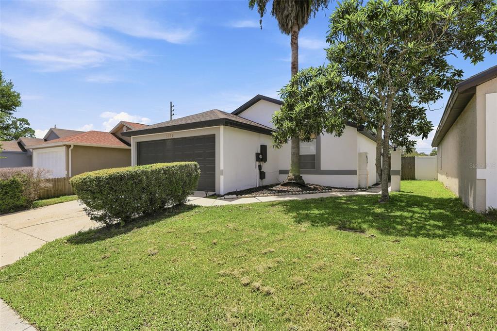 A single-story house with a white stucco exterior, a dark garage door, and a front lawn — 5230 FLORIDA HOLLY DRIVE, ORLANDO, FL