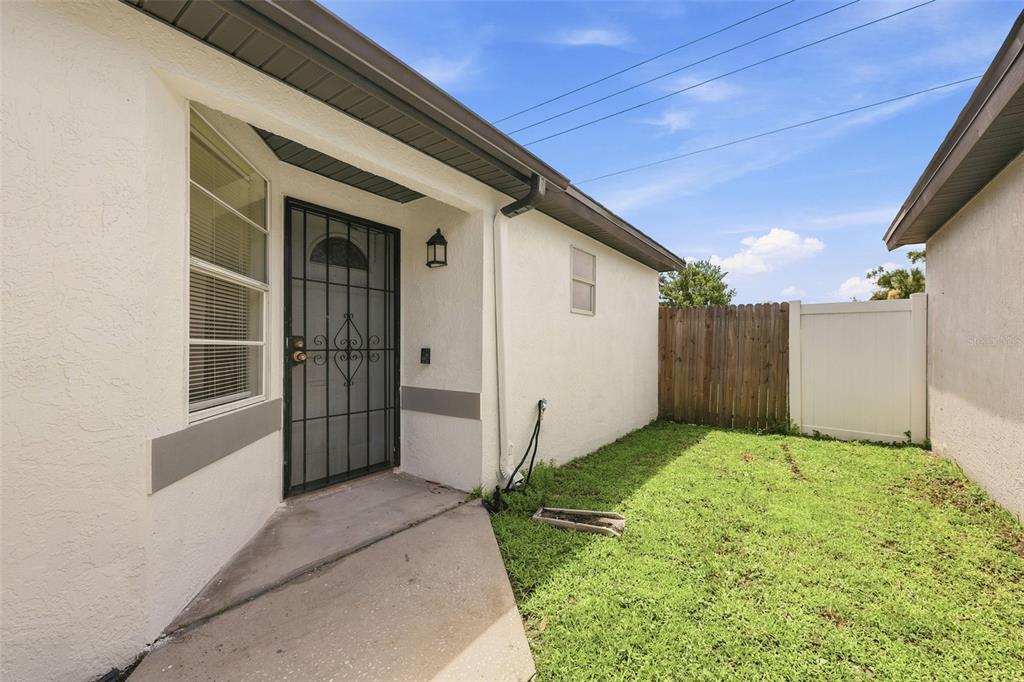 A concrete walkway leads to a front door with a black security gate and lawn — 5230 FLORIDA HOLLY DRIVE, ORLANDO, FL